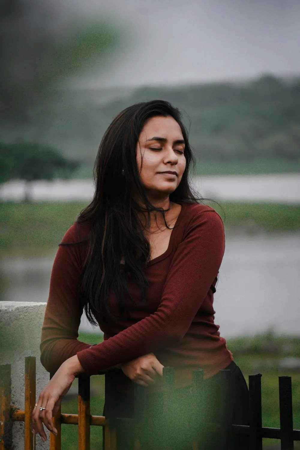 Woman in a Maroon Top Sitting Near the Lake on a Calm Day