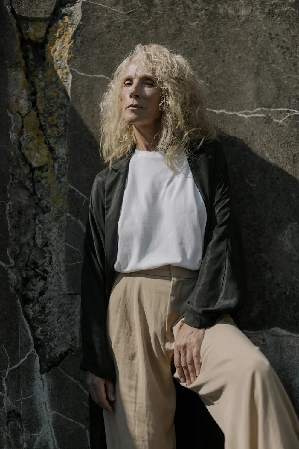 Woman in Neutral Fashion Leaning Against a Dark Stone Wall