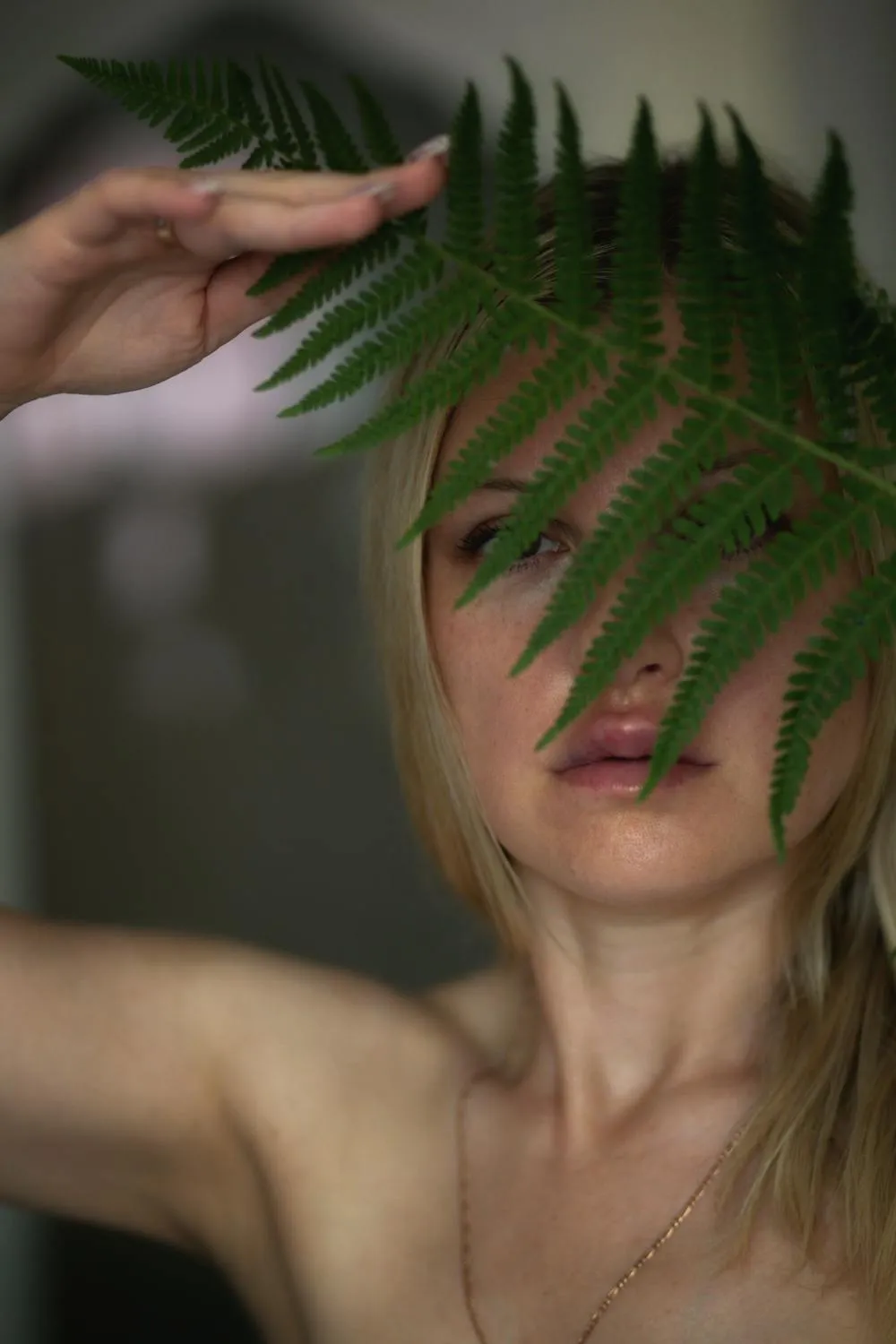 Woman Partially Hiding Her Face Behind a Fern Leaf Image