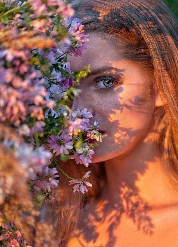 Woman Peeking Through Flowers with a Sunlit Face Wallpaper