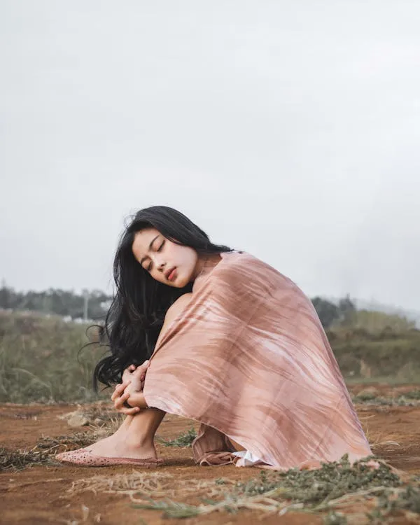 Woman in a Pink Dress Sitting Outdoors on a Grassy Field