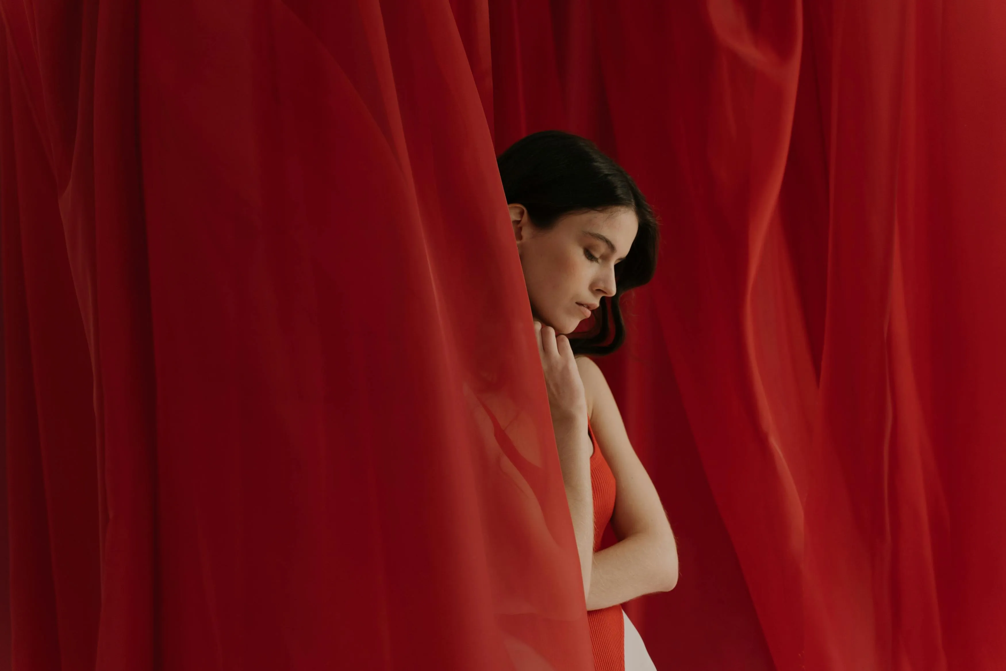 Woman Posing Near a Red Curtain and Looking Down Wallpaper