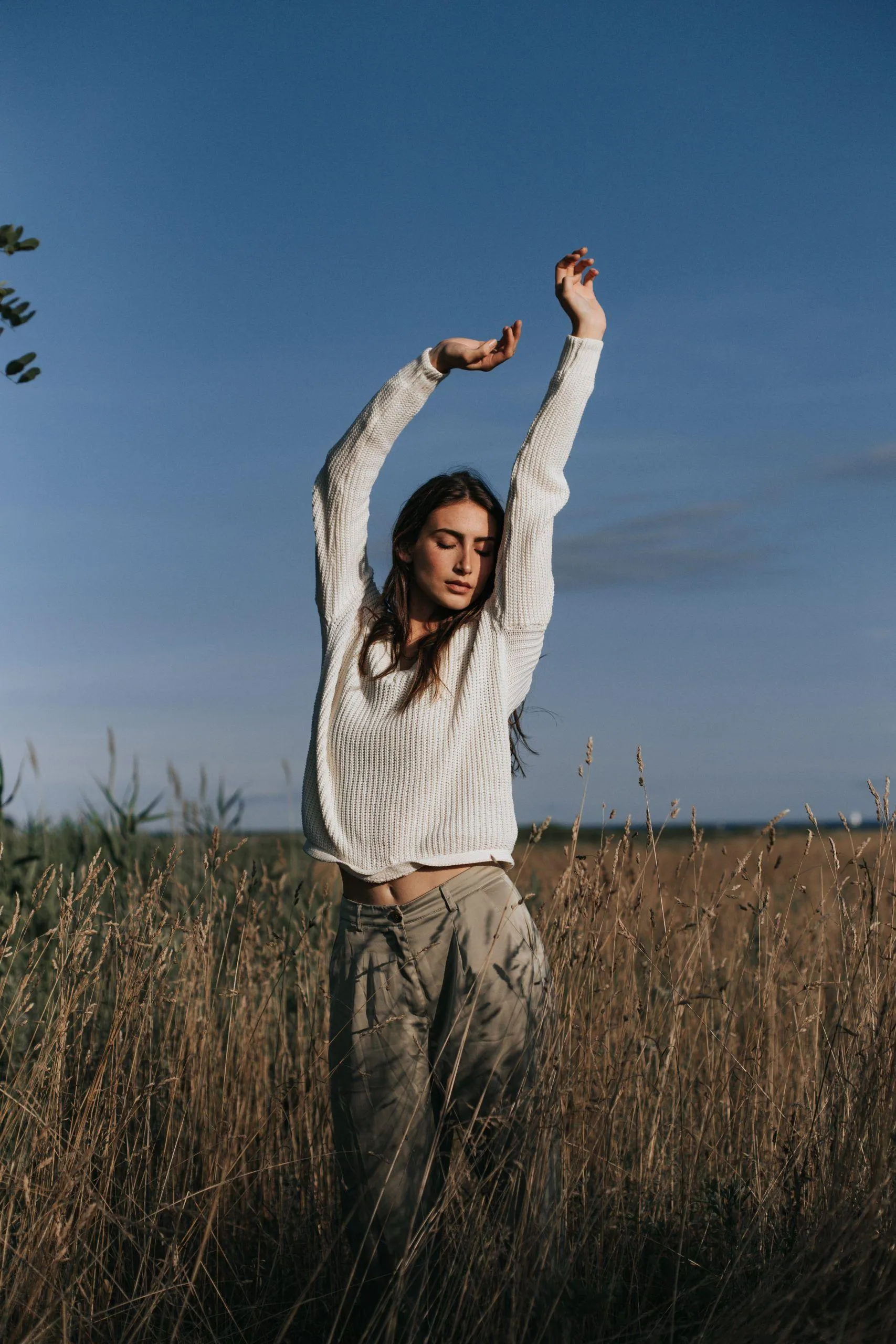 Woman Raising Arms Standing in a Field with a Blue Sky Image