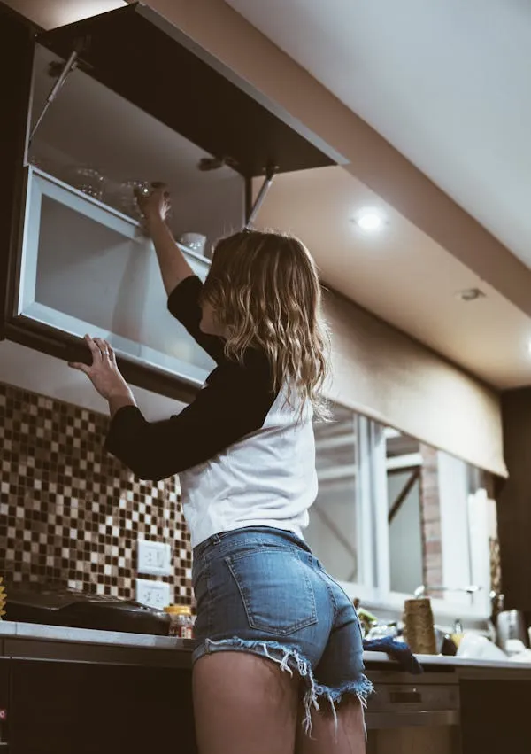 Woman Reaching a Cabinet Shelf in the Kitchen Wearing Shorts