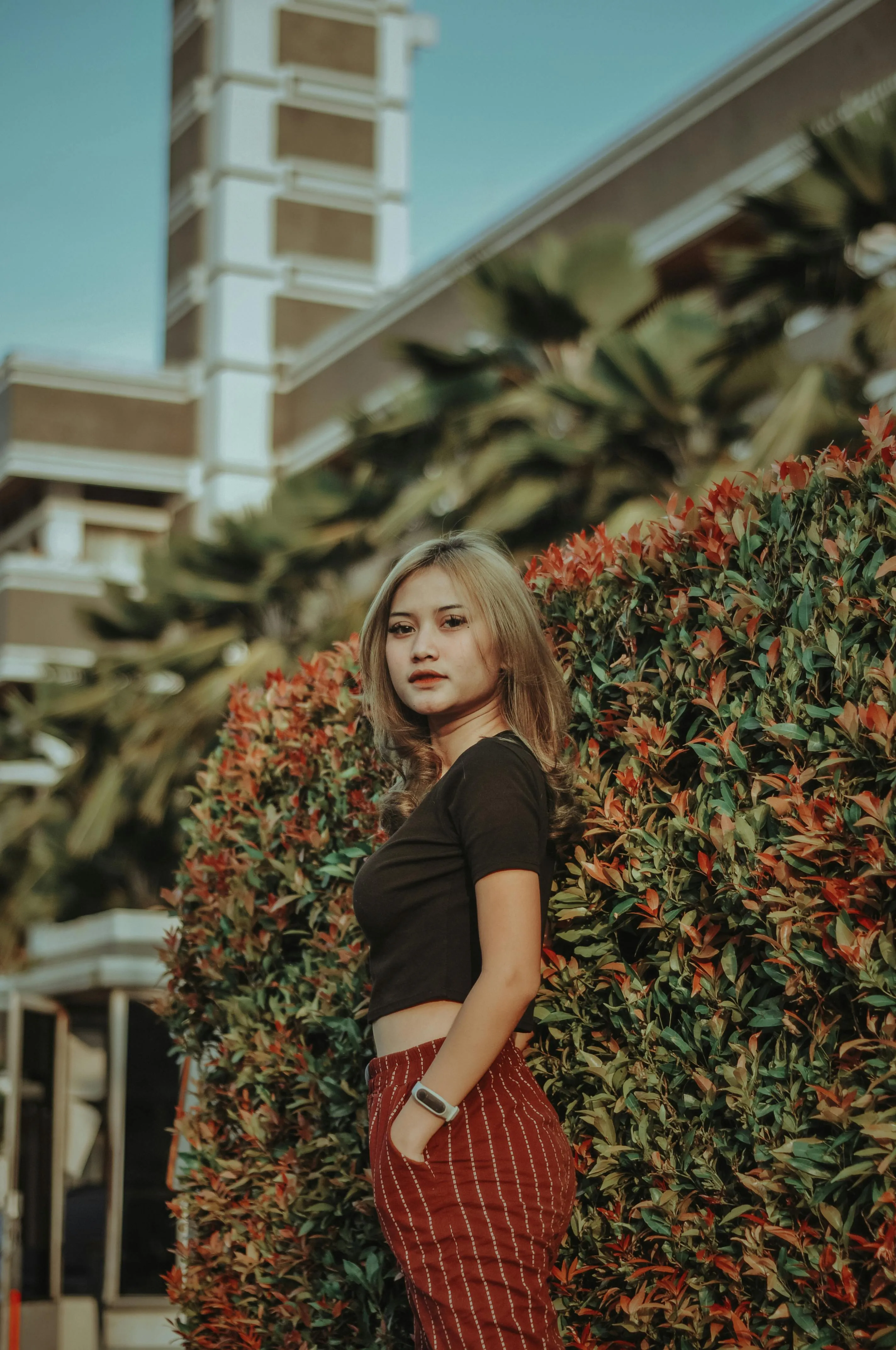 Woman in a Red Dress Standing Beside a Leafy Garden Wall