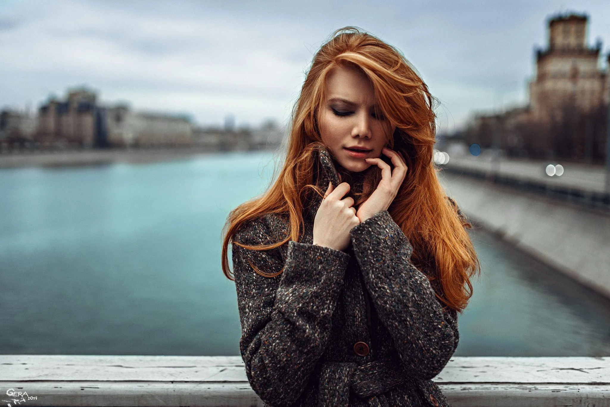 Woman with Red Hair Standing Near a River with a City View