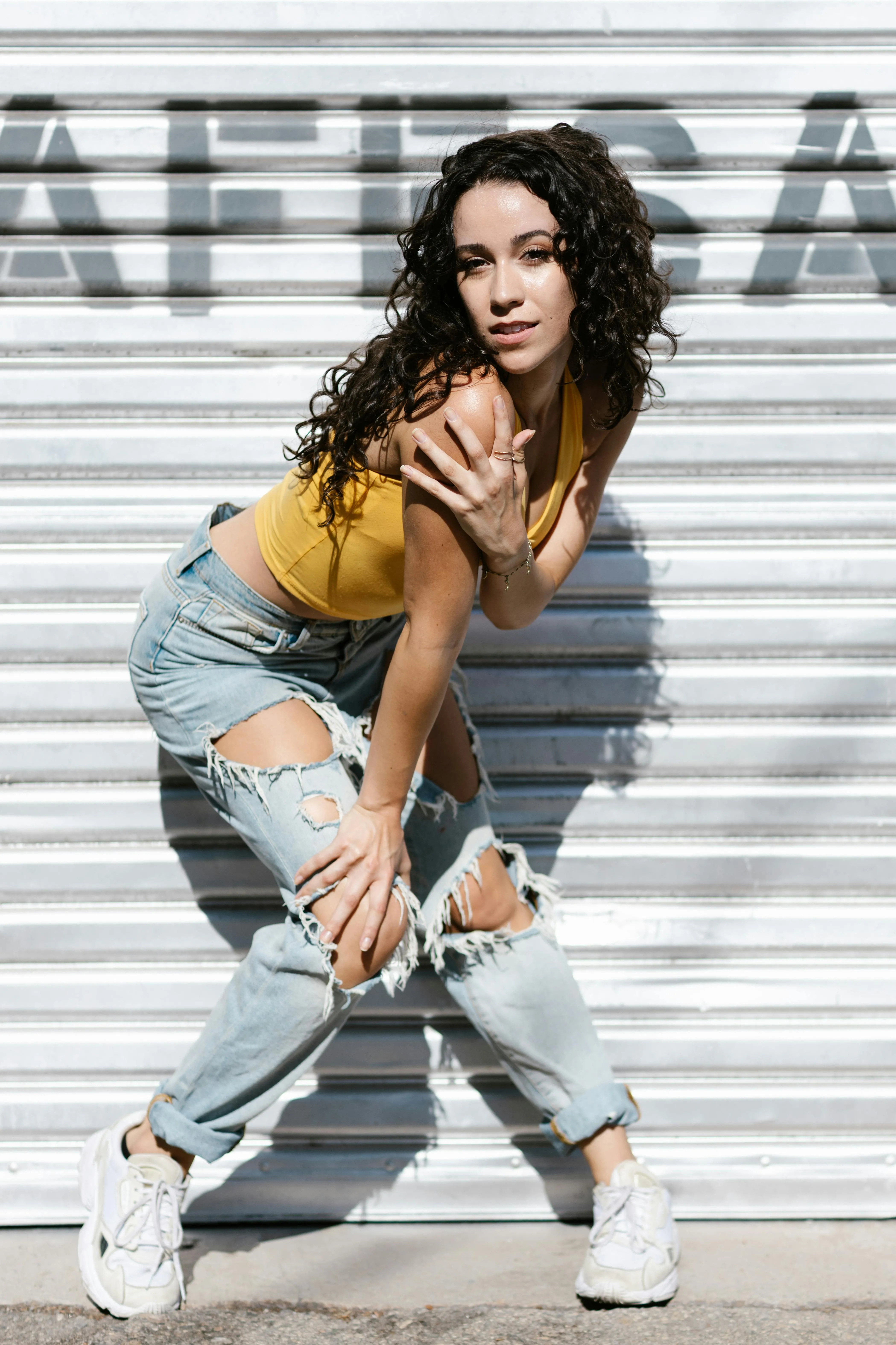 Woman in Ripped Jeans Crouching Near a Metal Gate Wallpaper