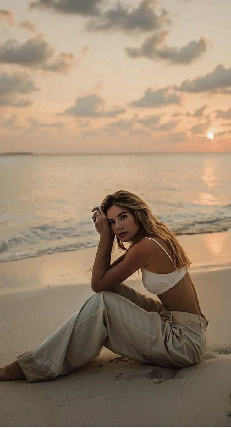 Woman in Silver Pants Sitting by the Ocean During Sunset
