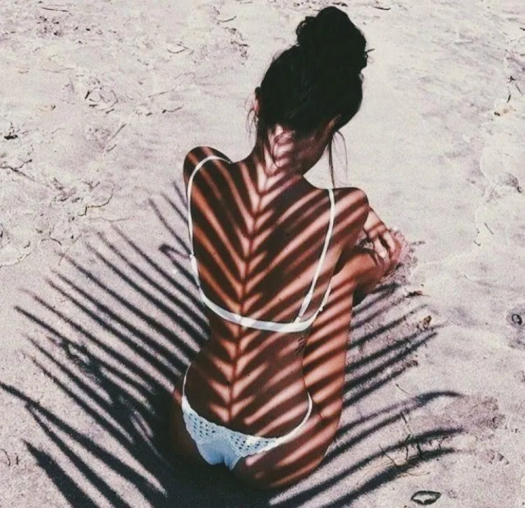 Woman Sitting on a Beach with Palm Leaf Shadows in a Bikini