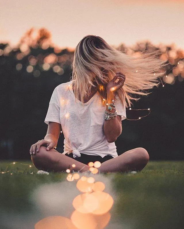 Woman Sitting Cross Legged in the Grass with Lights At Dusk