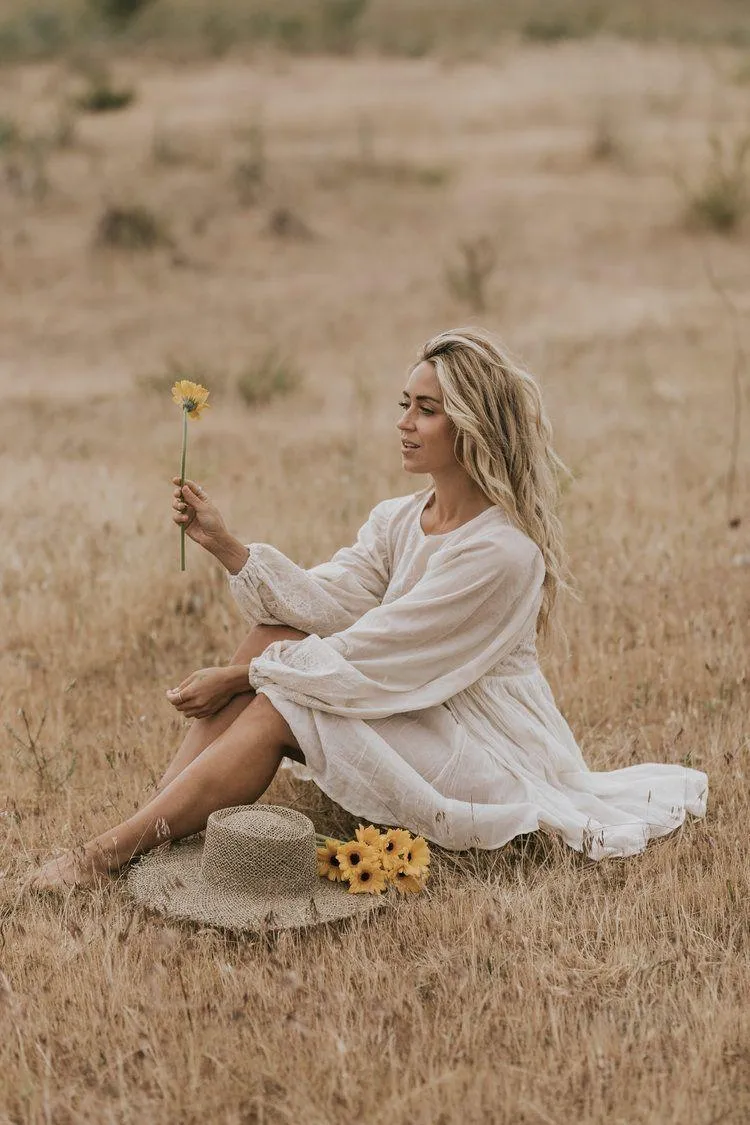 Woman Sitting in a Dry Field Holding a Sunflower Flower
