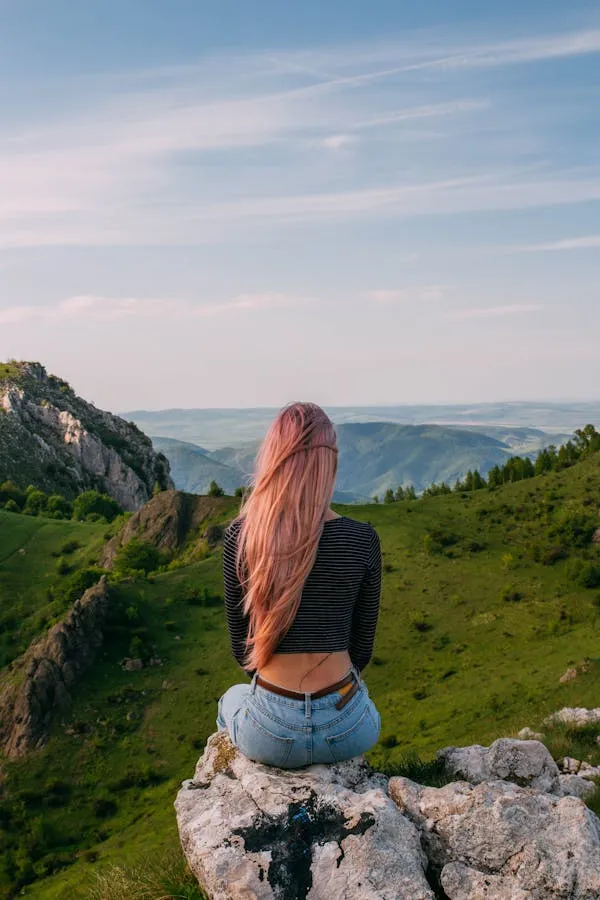 Woman Sitting on Rocks Looking At a Scenic Mountainous View