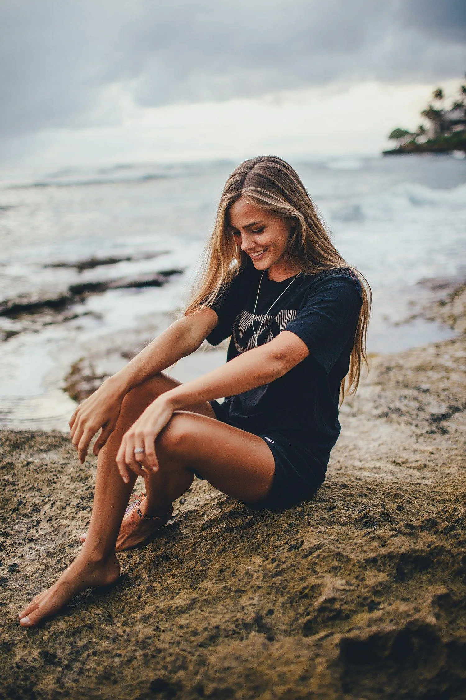 Woman Sitting on a Rocky Beach in a Black Dress and Relaxing