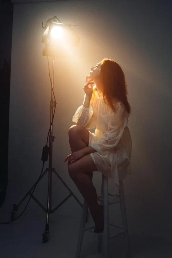 Woman Sitting on a Stool Under a Spotlight in a Dark Studio