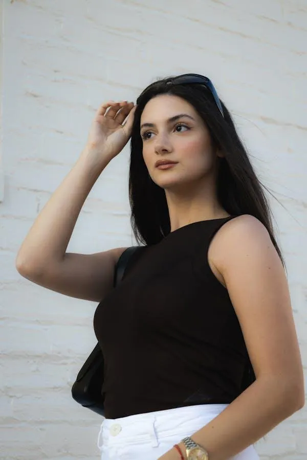 Woman in a Sleeveless Black Top Posing Against a White Wall