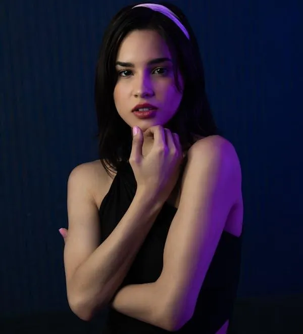 Woman in a Sleeveless Black Top Posing Under Blue Lighting
