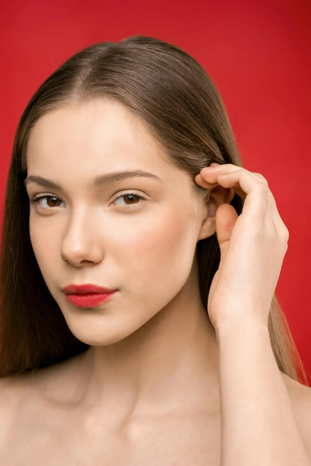 Woman with Smooth Skin Touches Her Hair in a Red Background