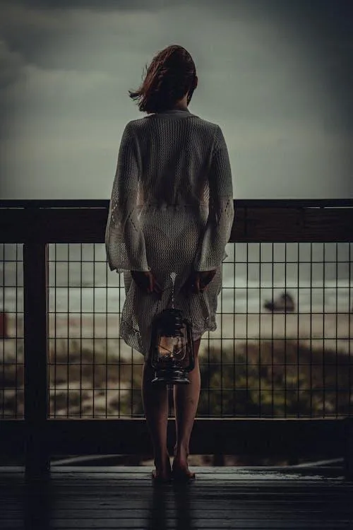 Woman Standing on a Balcony Facing Sunset in Warm Tones