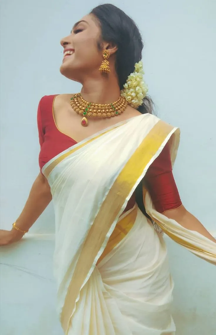 Woman standing near wall wearing Onam saree with red blouse