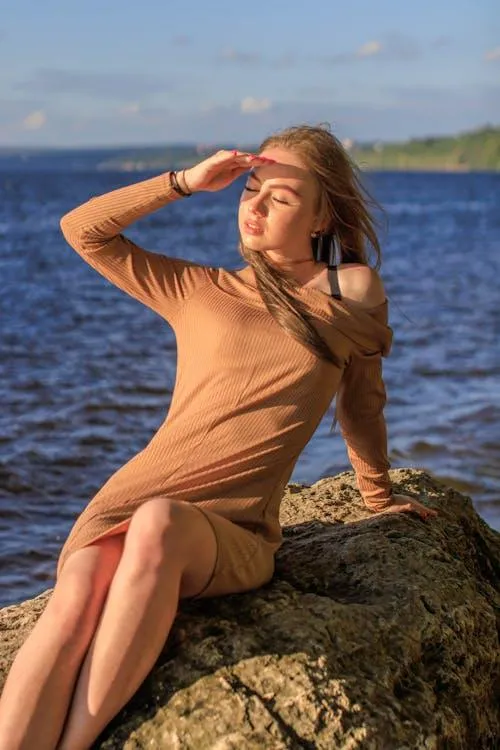 Woman in a Tan Dress Posing on a Rock Beside a Calm Lake