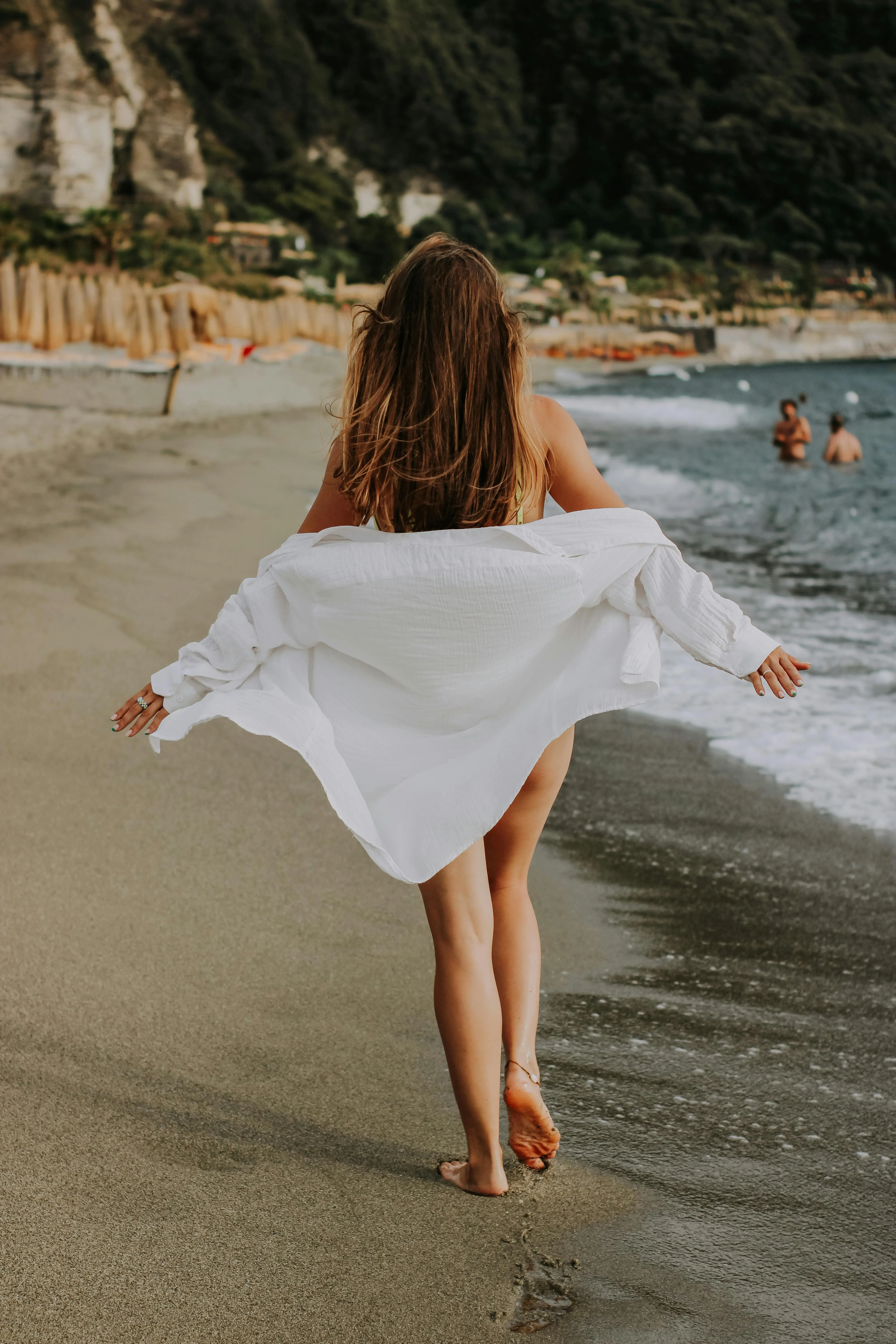 Woman Walking Along the Beach Holding White Shirt Wallpaper
