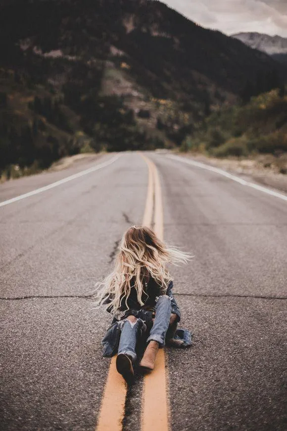 Woman Walking Down an Empty Road Surrounded by Mountains