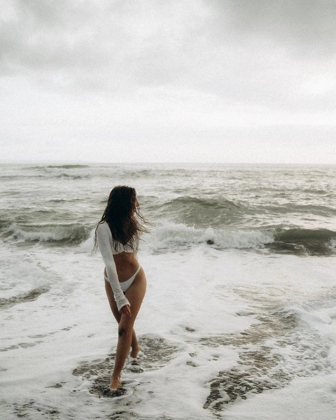Woman Walking Into the Ocean Waves on a Cloudy Day Wallpaper
