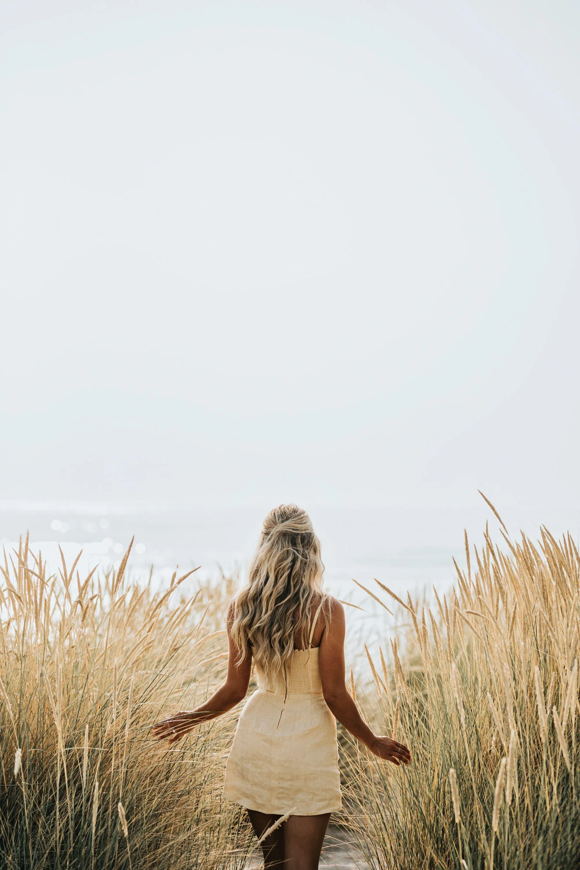 Woman Walking in Tall Grass Looking Out To a Bright Sky
