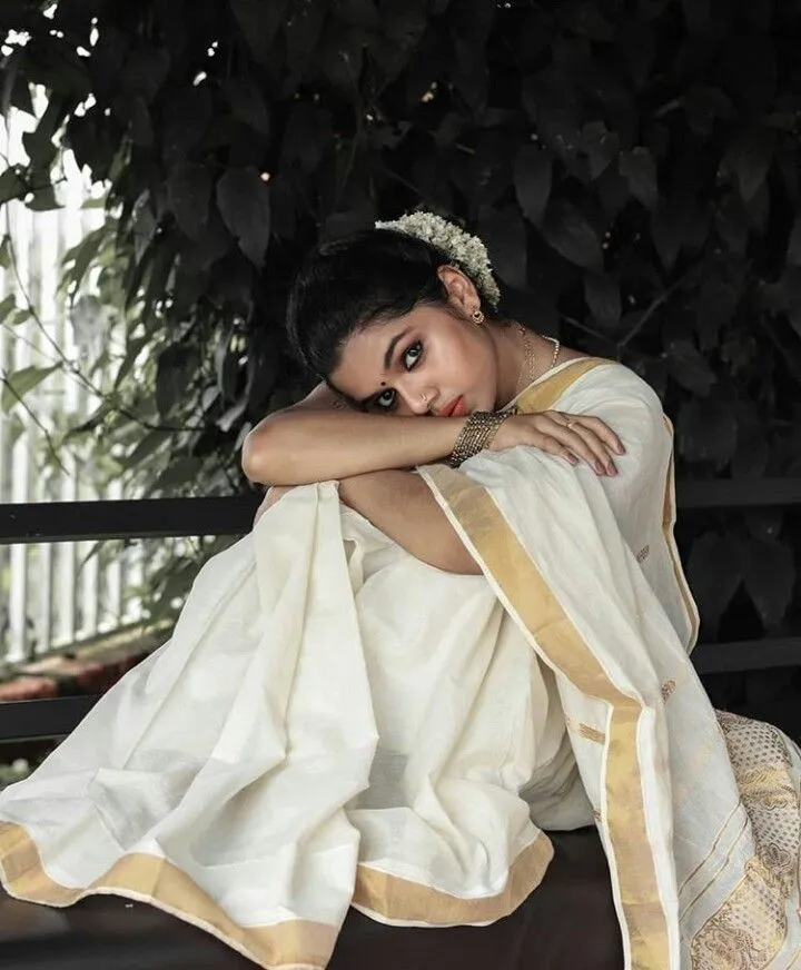 Woman wearing a Kerala Kasavu Saree sitting near a tree
