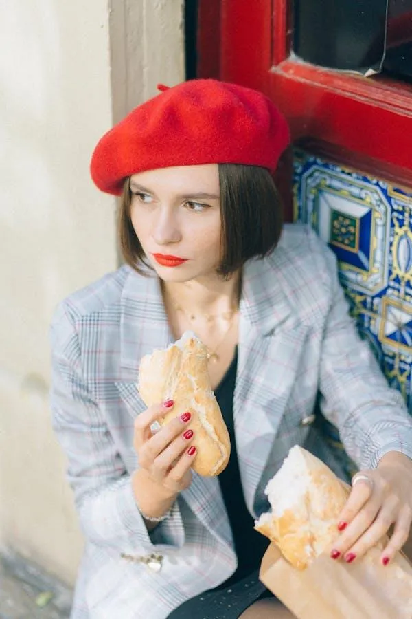 Woman Wearing a Red Beret Eating Sandwich by a Colorful Wall