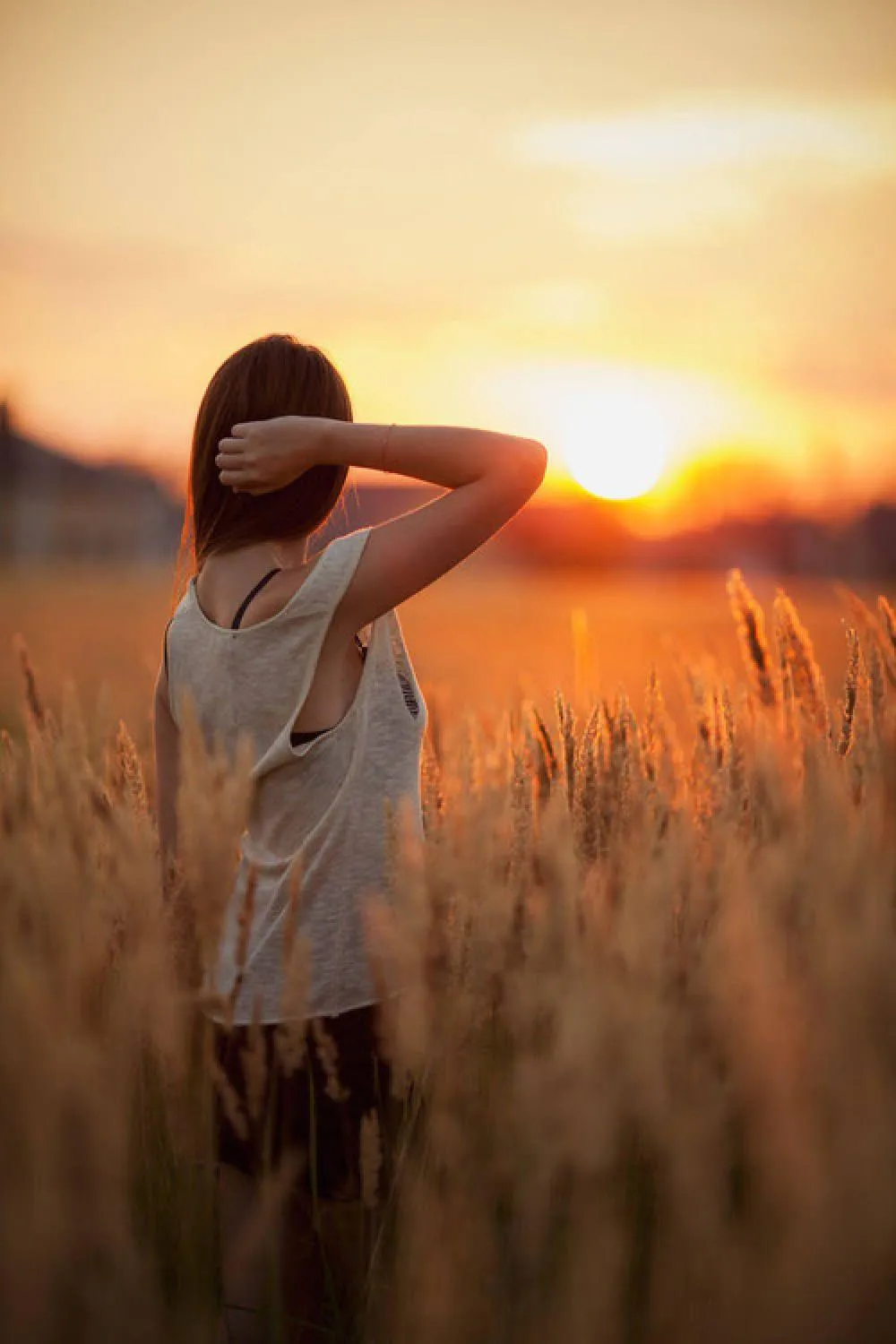 Woman in a Wheat Field At Sunset with Hands Behind Her Head