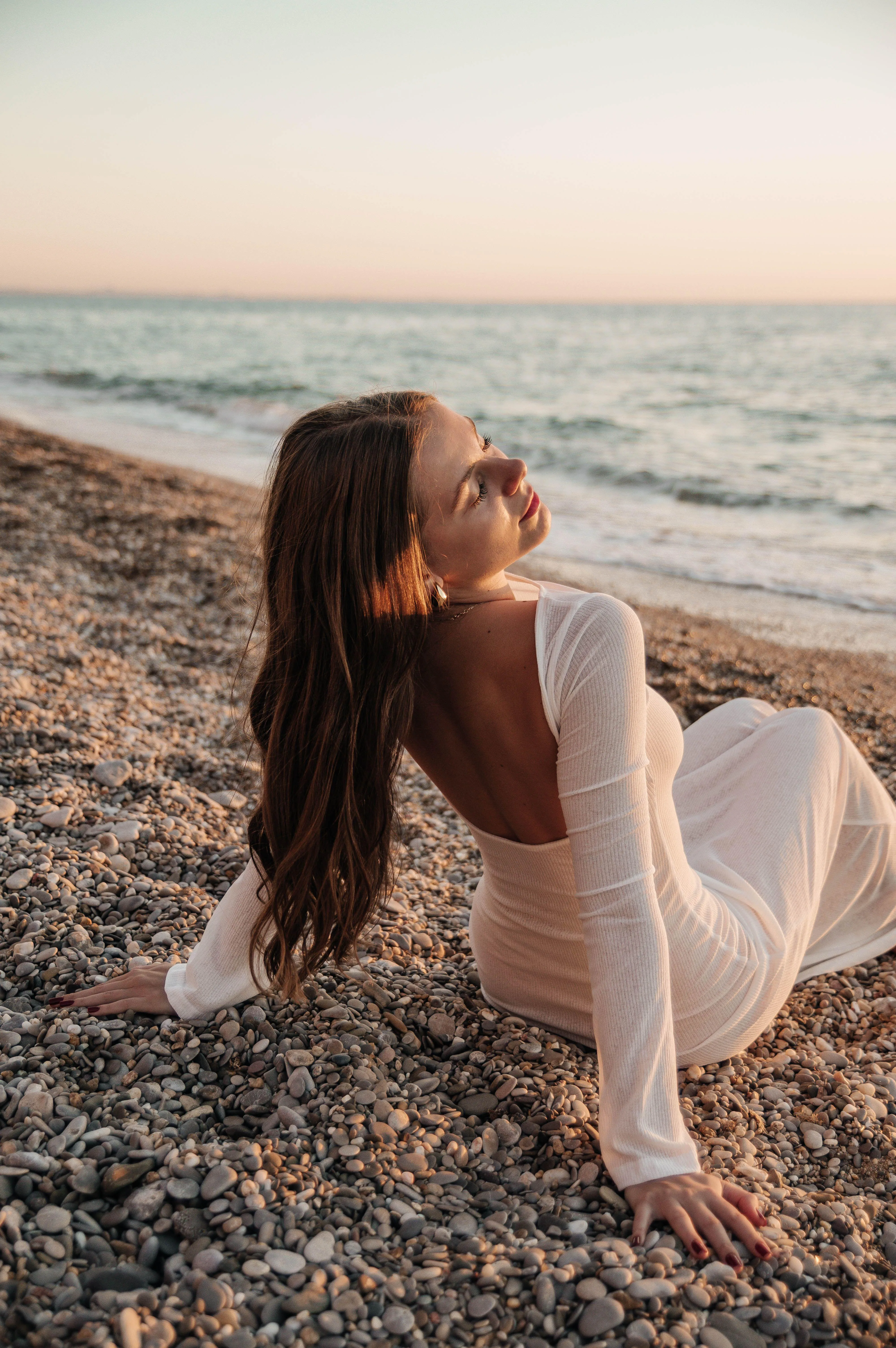 Woman in a White Dress Sitting on Beach During Golden Hour