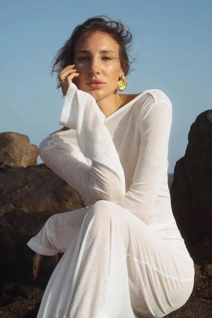 Woman in a White Dress Sitting on Rocks Under a Clear Sky