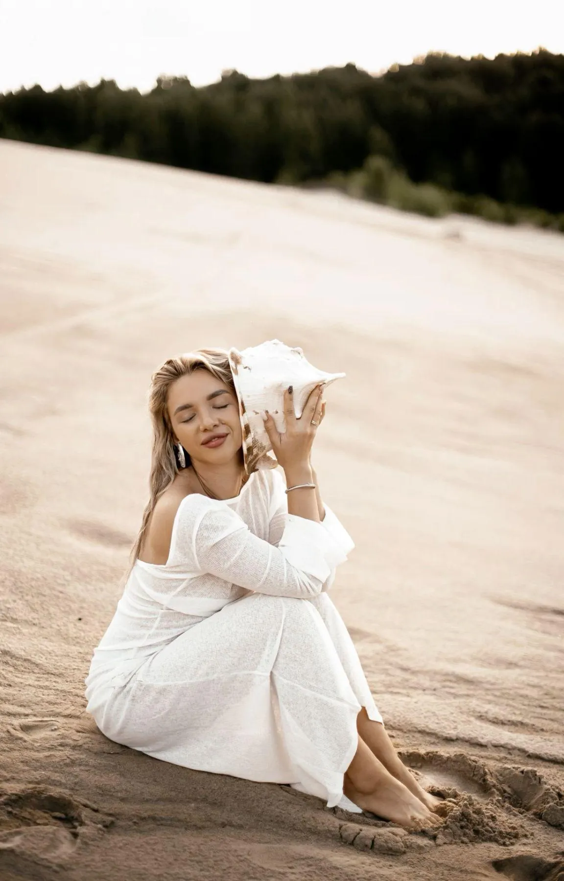 Woman in White Dress Sitting on Sand with Dreamy Expression
