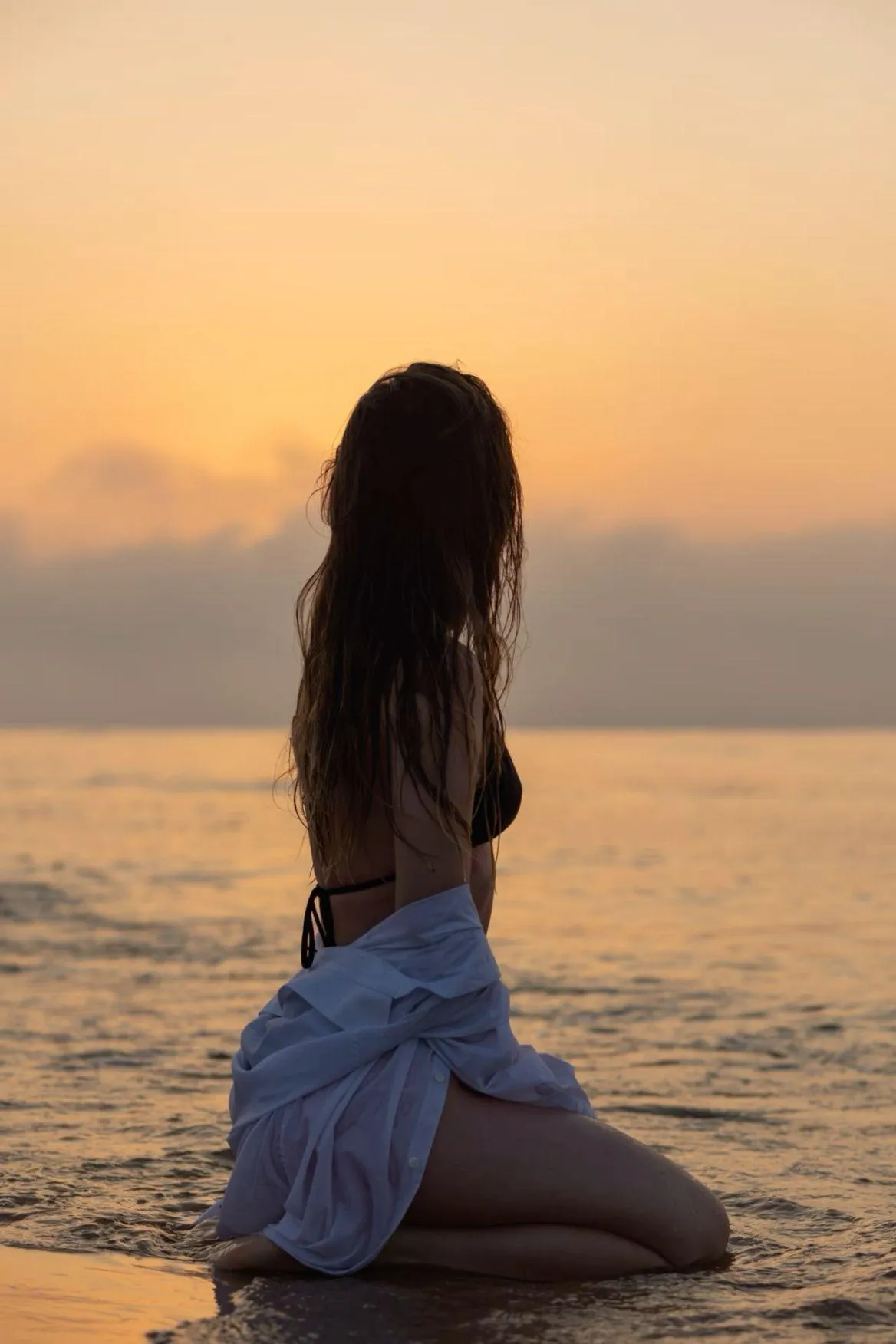 Woman in a White Dress Sitting on the Beach At Sunset Image