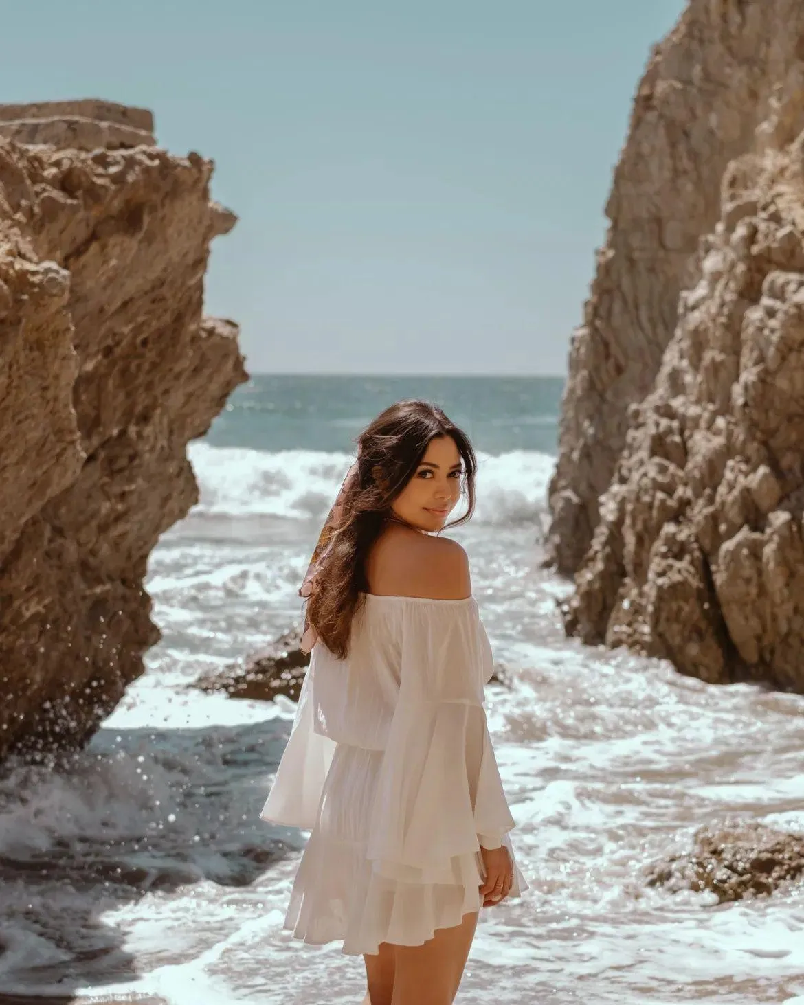 Woman in a White Dress Standing on Rocky Beach by the Ocean