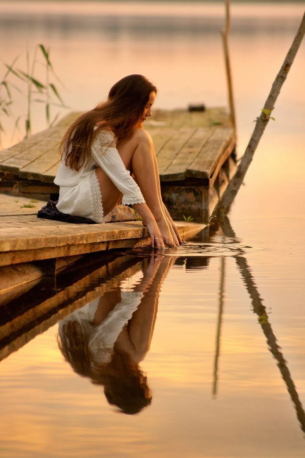 Woman in a White Dress Touching Water in a Peaceful Sunset