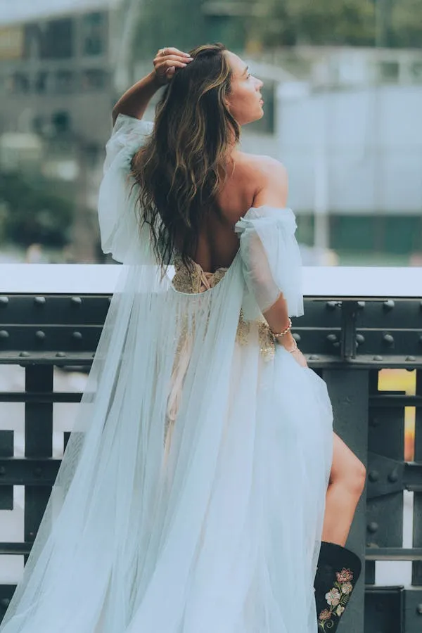 Woman in a White Gown on Balcony Looking Over Cityscape