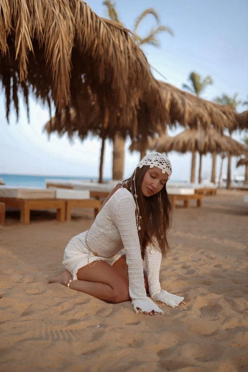 Woman in White Outfit Sitting on the Beach Under a Palm Tree