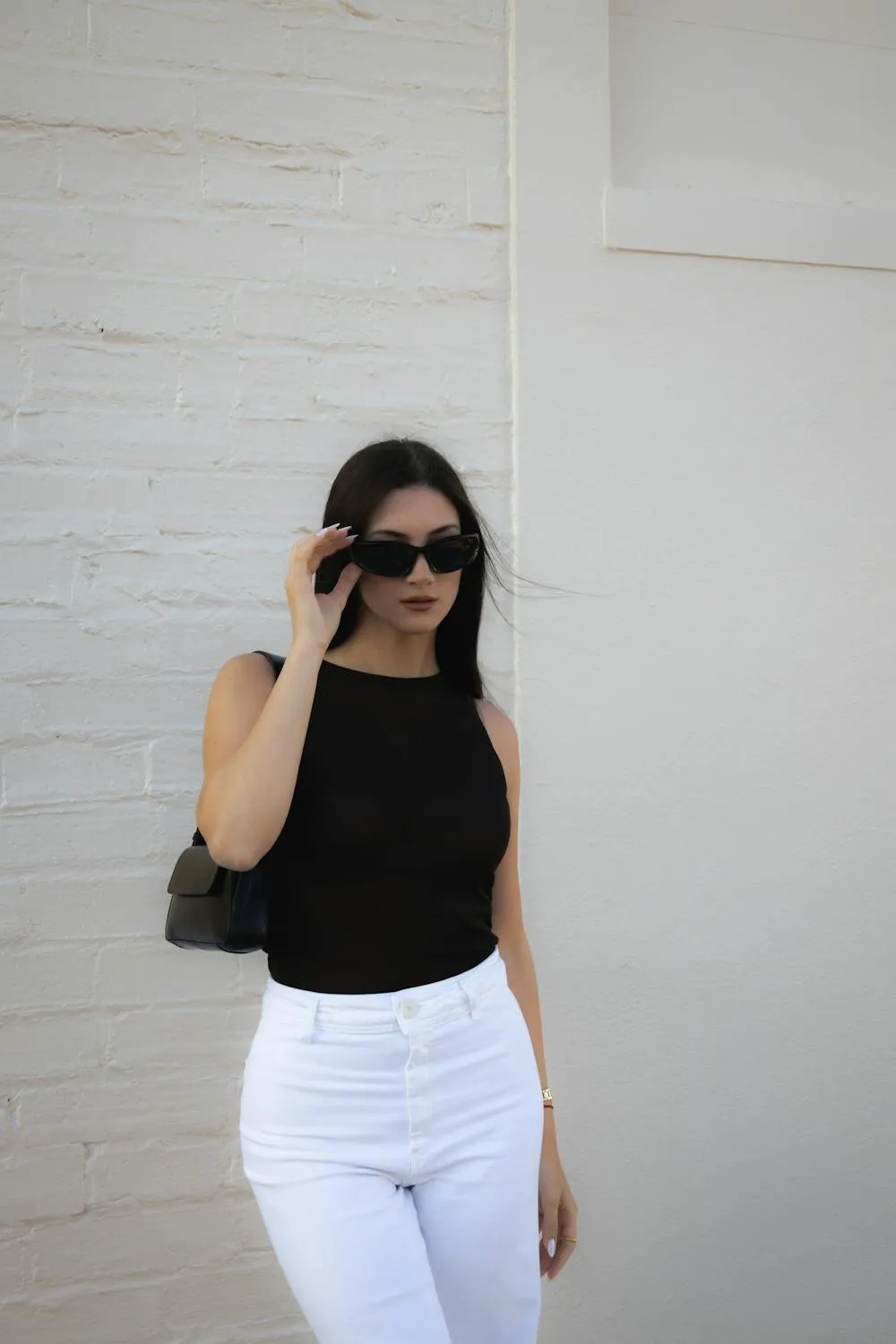 Woman in White Pants and a Black Top Posing by a White Wall