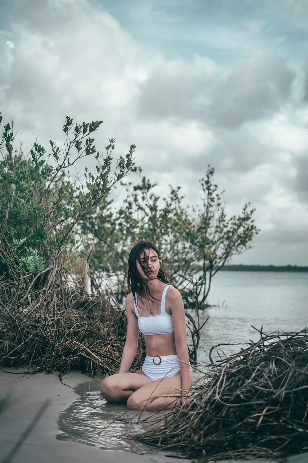 Woman in a White Swimsuit Sitting on a Rock Near the Water