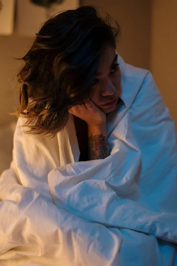Woman Wrapped in White Sheets Sitting on Bed in Soft Light