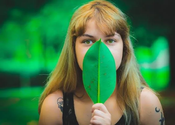 Young Woman Hiding Behind a Green Leaf in a Nature Scene