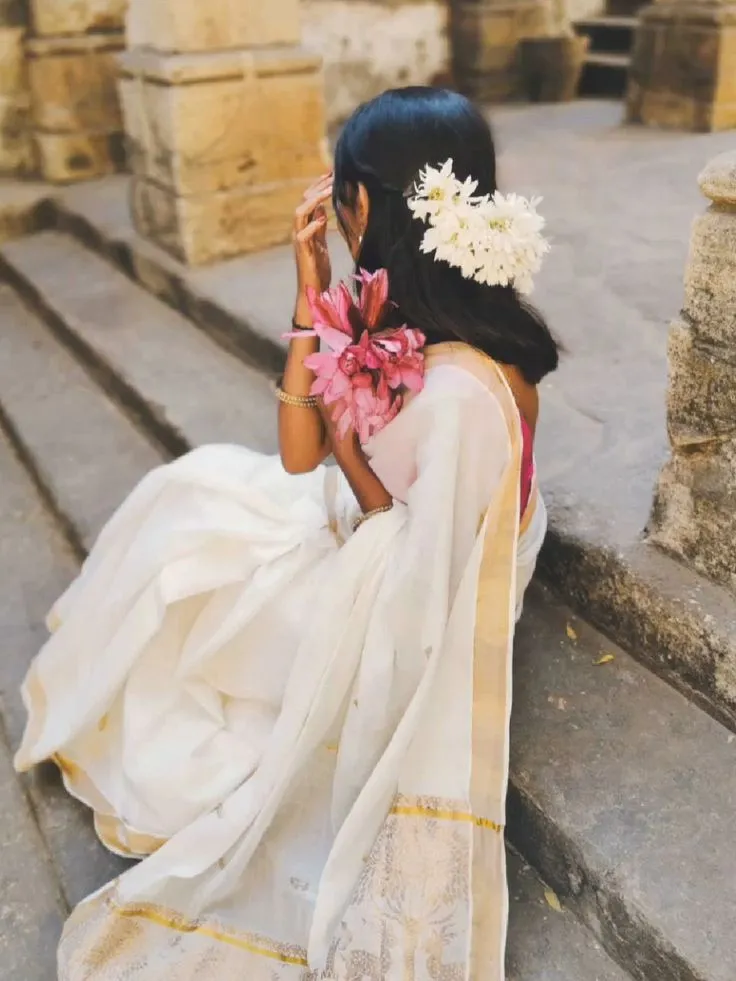 Young woman holding a pink flower wearing a white saree