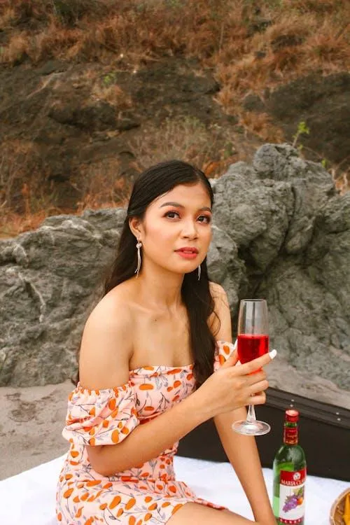 Young Woman Holding a Drink and Sitting on Rocks Outside