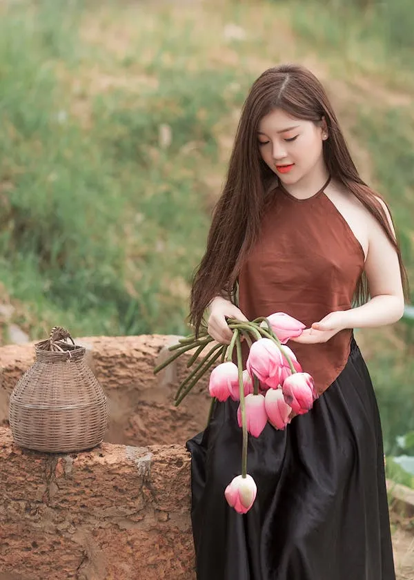 Young Woman Holding Flowers and Standing in a Green Field