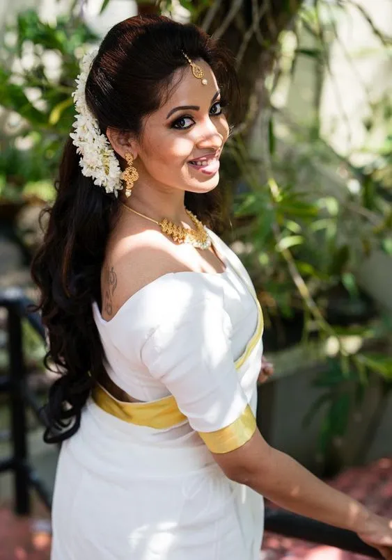 Young woman in a kasave saree standing near a green tree