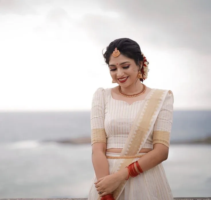 Young woman in a Kasavu saree standing near water wallpaper