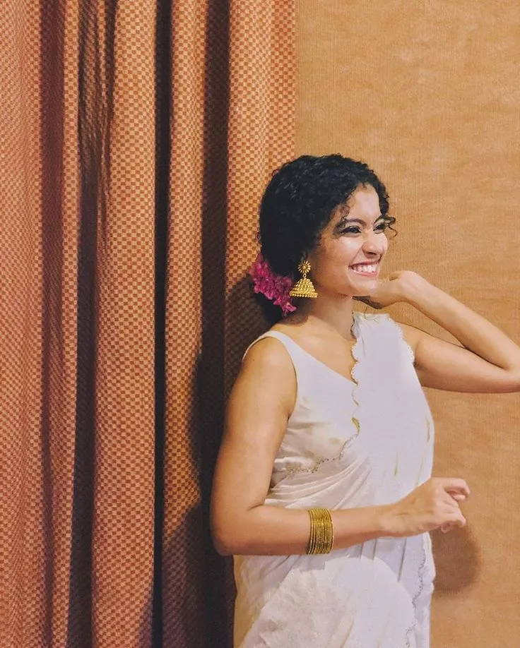 Young woman in a Kerala saree standing near a red curtain