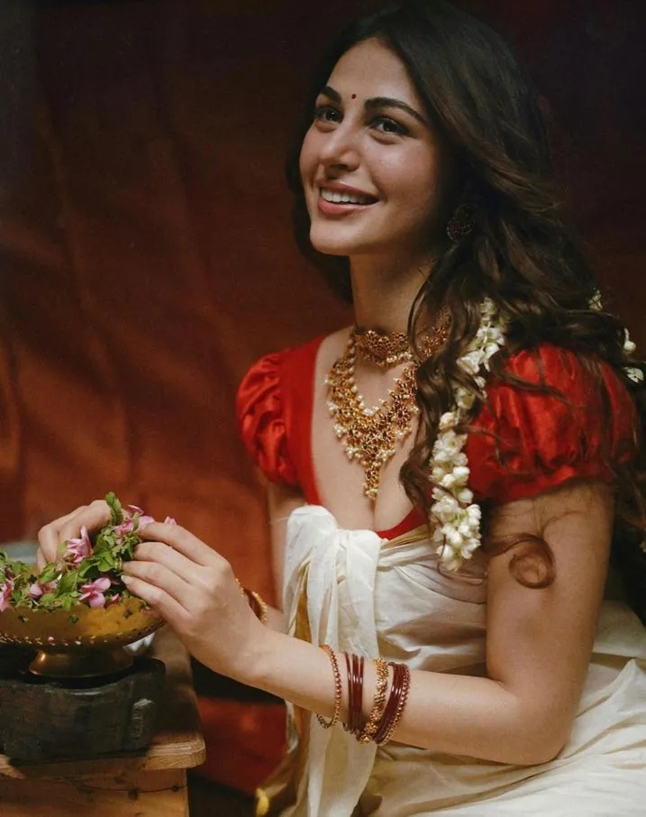 Young woman in a white and red saree holding a flower image